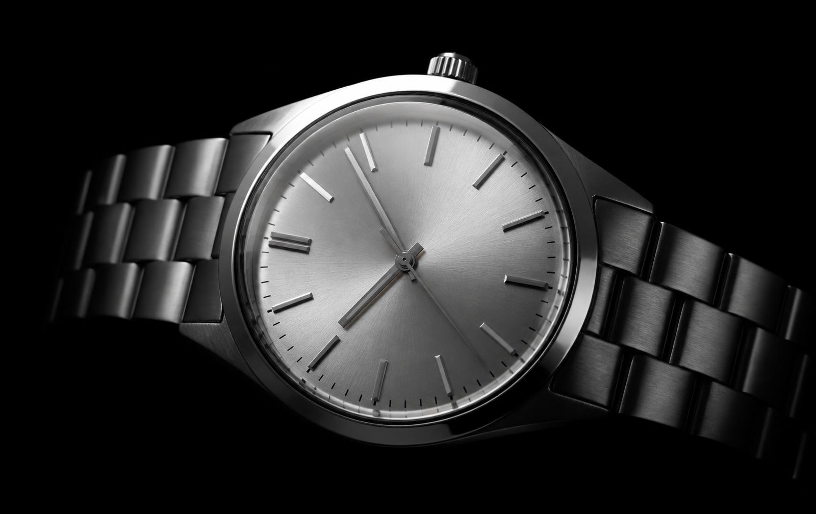 A vintage stainless steel watch lit by a single cold highlight against a near-black background